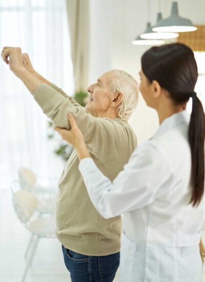 Female doctor helping an elderly man to do exercises in room Female doctor helping an elderly man to do exercises in room